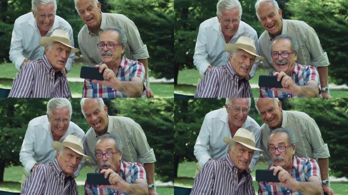 一群老人在公园里享受户外天气。老年男性朋友在智能手机上拍照时开玩笑地做鬼脸。积极活泼的老年人使用技术