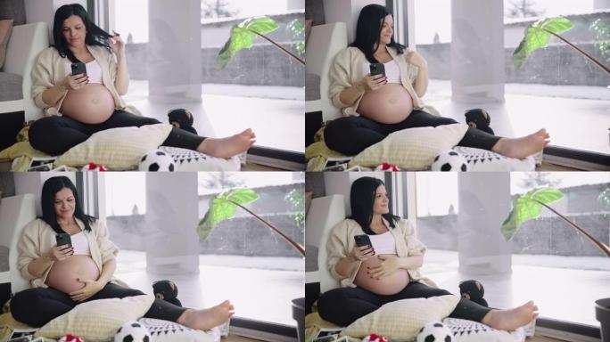 怀孕后期的DS女人在家里使用智能手机时爱抚着腹部