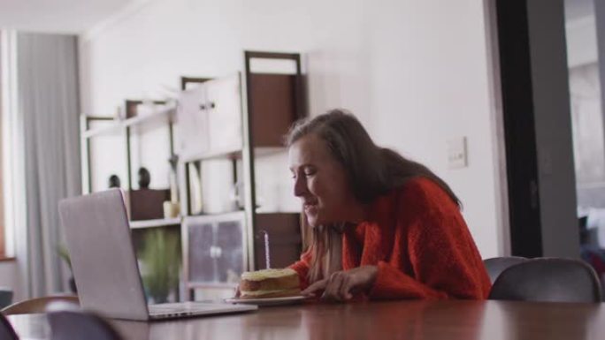 女人在家里的笔记本电脑上进行视频聊天时，在蛋糕上吹蜡烛