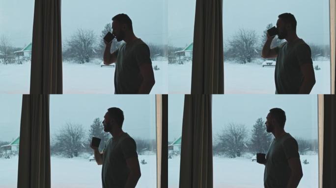 男人喝热茶，看着雪落下