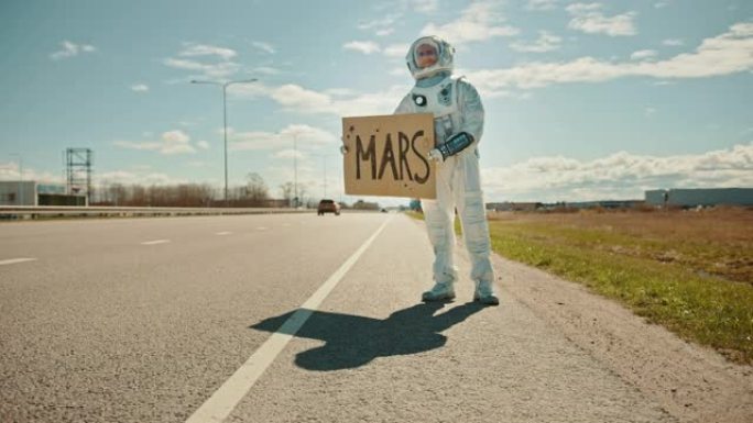 穿着宇航服的人站在路边，举着上面写着火星的标志。宇航员想搭便车。太空人穿着未来主义的西装，手上有技术