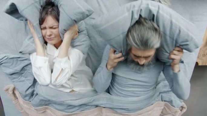 恼怒的夫妇打架表示愤怒躺在床上，一起用枕头遮住头，避免交流