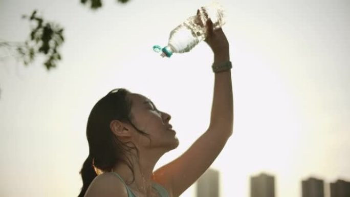 女跑步者在锻炼后往脸上倒水。瓶子里的冷水溅到绿色背景下的女孩脸上。