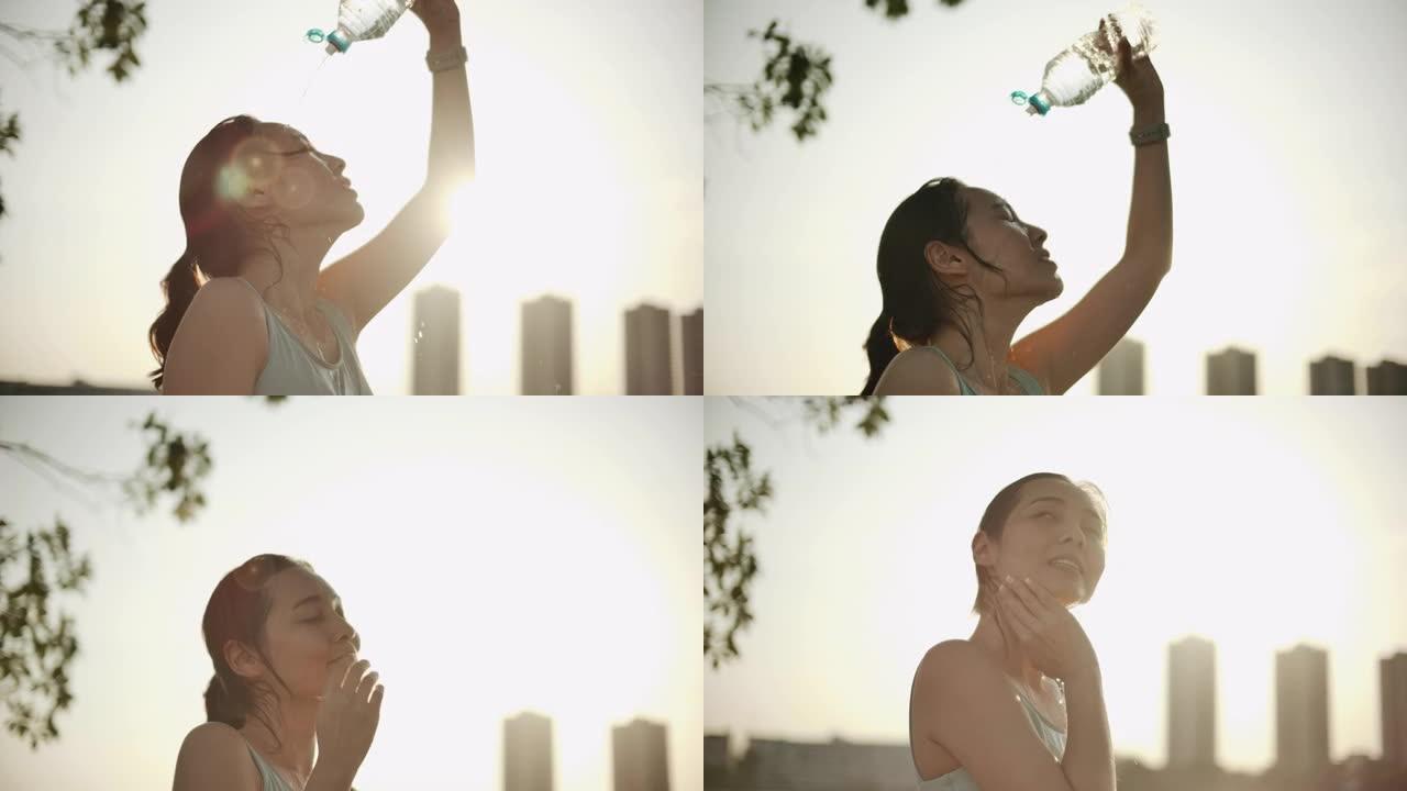 女跑步者在锻炼后往脸上倒水。瓶子里的冷水溅到绿色背景下的女孩脸上。