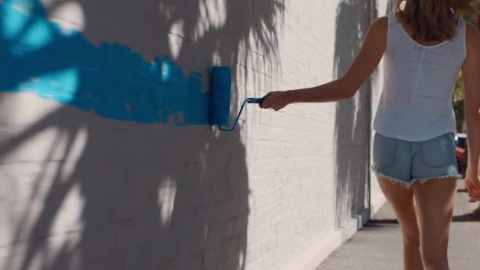 年轻艺术家女人用蓝色油漆画墙走在城市街道上独立女性享受城市涂鸦艺术表达