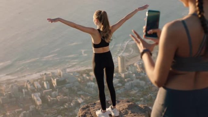女朋友用智能手机相机在山顶拍照美丽的年轻女子用手机在社交媒体上分享徒步旅行冒险