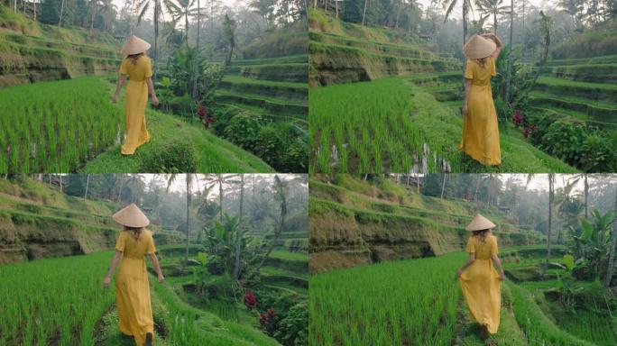 穿着黄色连衣裙戴帽子的稻田旅行女人探索郁郁葱葱的绿色大米露台漫步在文化景观中穿越巴厘岛印度尼西亚发现