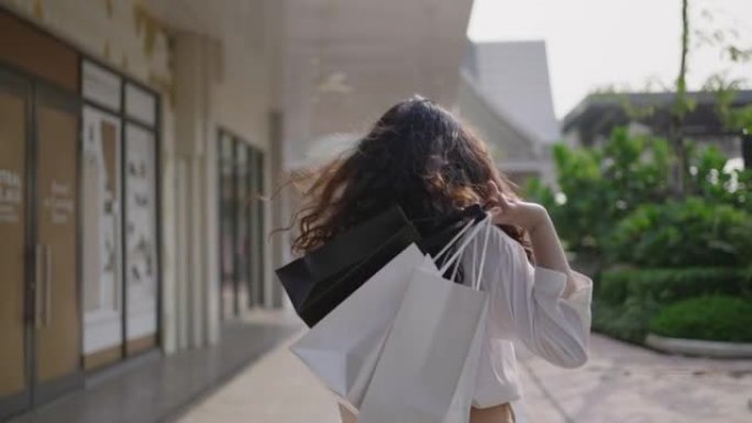 亚洲女人走在购物袋。微笑的女孩在镜头前调情
