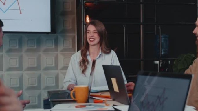 快乐的年轻25-30岁的女首席执行官、执行经理讲话，笑着与团队一起在办公桌前开会慢动作。