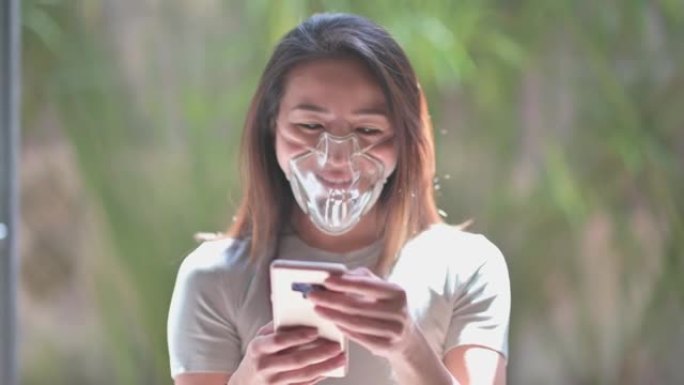 亚洲中国美丽的女人与透明保护面罩看她的智能手机短信微笑