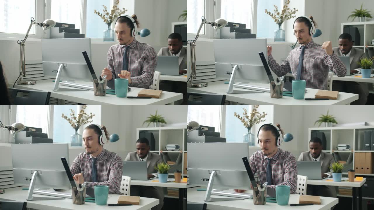 戴着耳机跳舞的创意年轻人在办公室的办公桌上与电脑一起工作