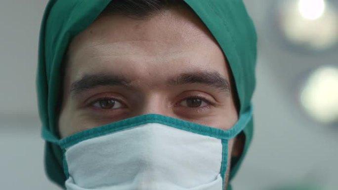 一位戴着口罩的男性医务人员在手术室里穿着医生的制服专注于他的眼睛，传达了住院治疗的概念。
