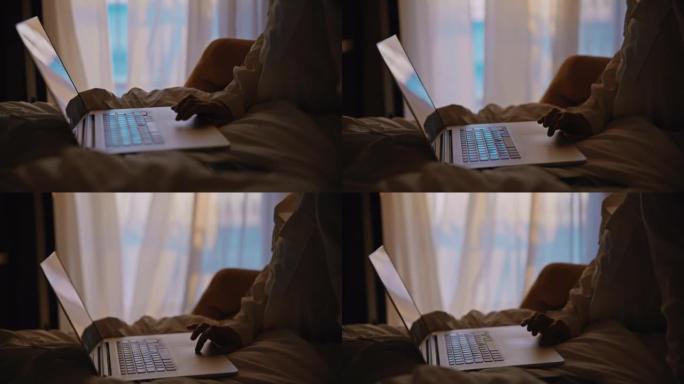 女人坐在酒店房间的床上，用她的笔记本电脑，透明的窗帘在背景中随风移动