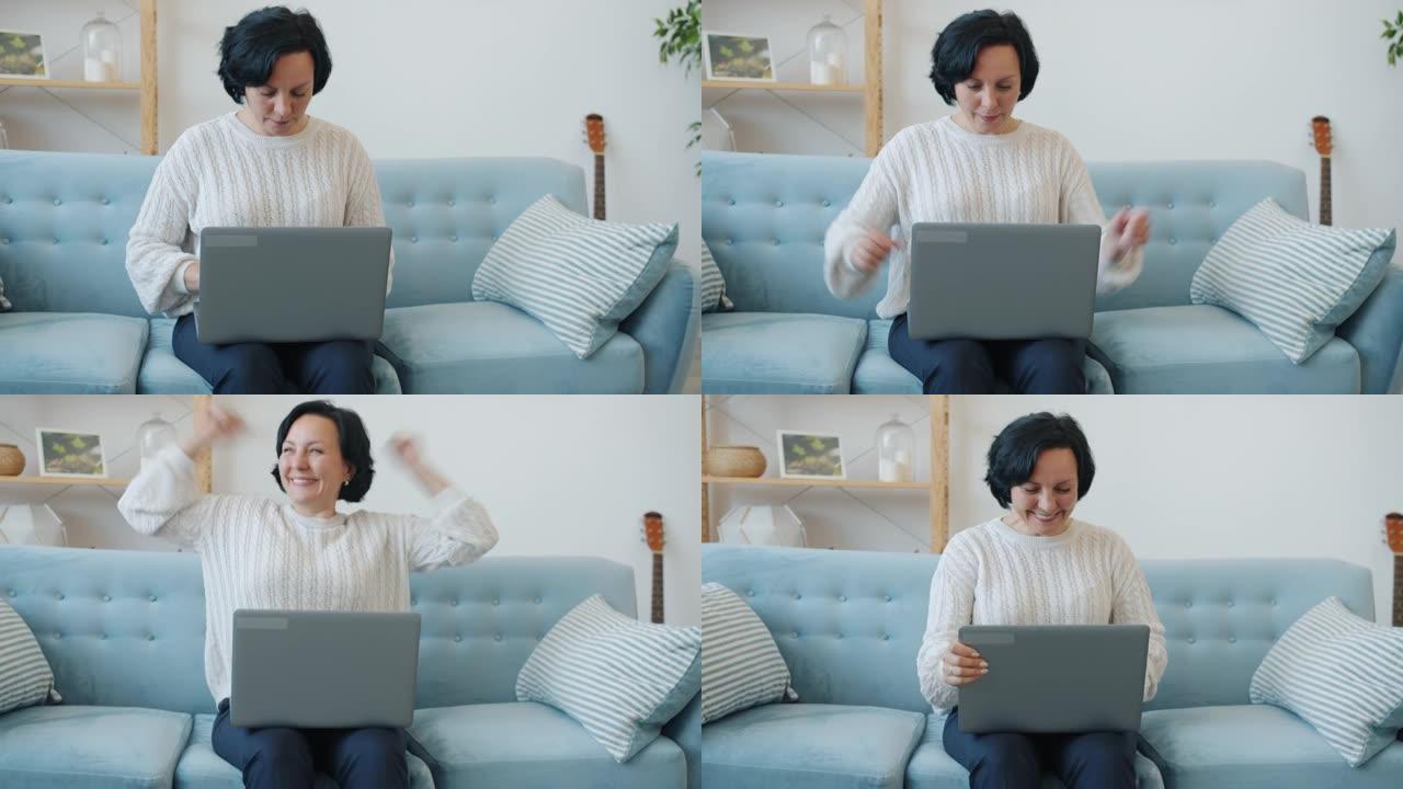 成熟的女人使用笔记本电脑打字，然后享受庆祝成功和在家微笑的好消息