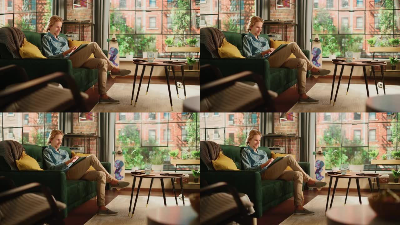 年轻英俊的成年男子坐在阁楼公寓的沙发上，在家用平板电脑工作。创意男性查看社交媒体，浏览互联网。从大窗