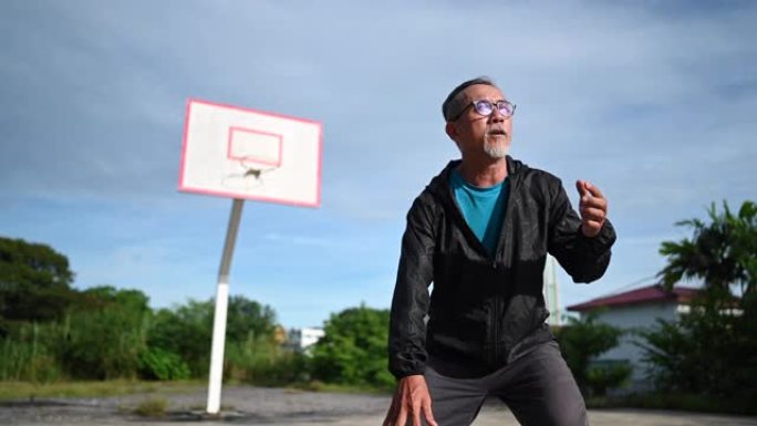 一名亚洲华裔资深男子上午在篮球场练习篮球赛