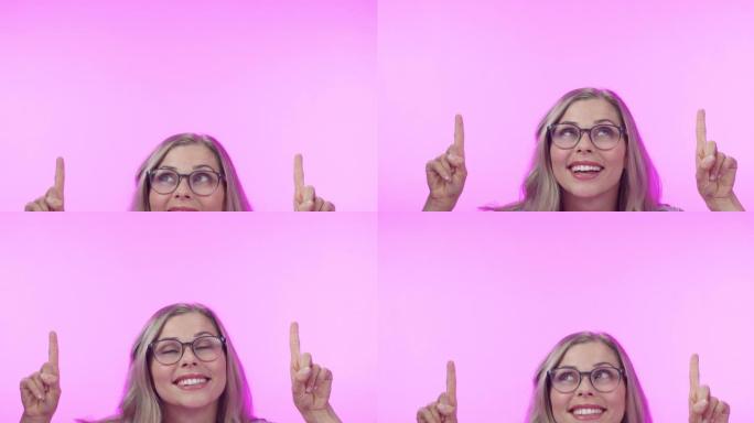 4k视频片段，一位迷人的年轻女子指着粉红色工作室背景下的复制空间