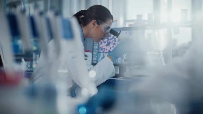 医学研究实验室: 护目镜的女科学家在显微镜下看，第二位科学家拿着带有生化物质的玻璃器皿。先进的医学科