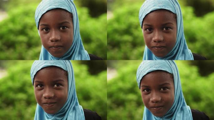 一个害羞的地道的非洲小女孩对着镜头微笑的特写肖像，背景是模糊的绿色。代表未来、希望和接受的黑人女性孩
