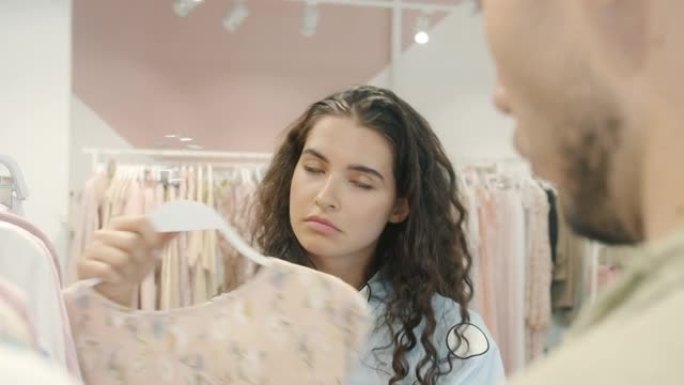 年轻女子在商店里选择衣服并与男人交谈的肖像表达情感