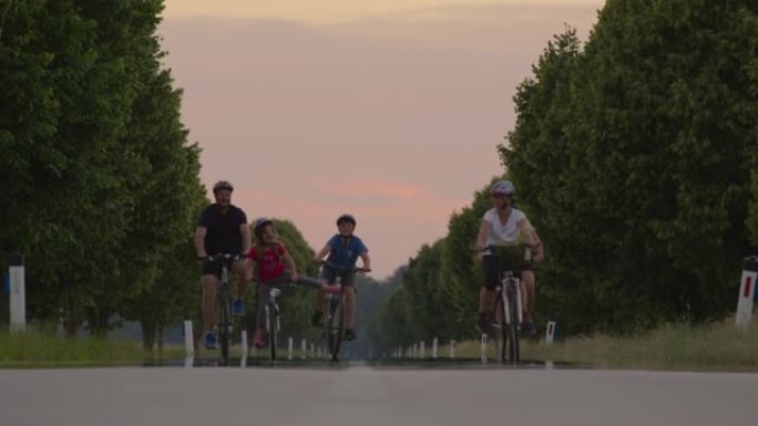 SLO MO家族在绿树成荫的道路上骑自行车时，举起手来。