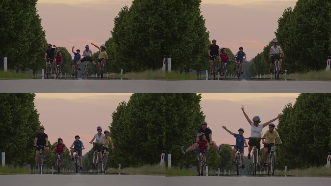 SLO MO家族在绿树成荫的道路上骑自行车时，举起手来。