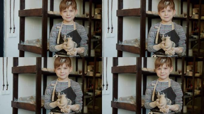 陶艺工作室里可爱的脏脸孩子拿着手工花瓶的慢动作肖像