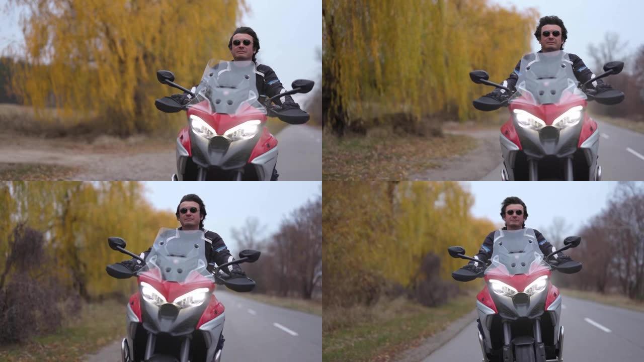 摩托车旅行。男子驾驶运动旅行摩托车骑在公路上。摩托车之旅。背景上的秋天树木