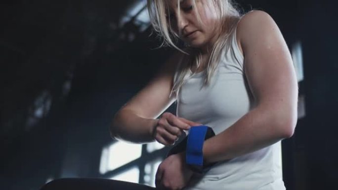 低角度年轻美丽的女性举重运动员戴上腕带，为在现代健身房锻炼做准备。