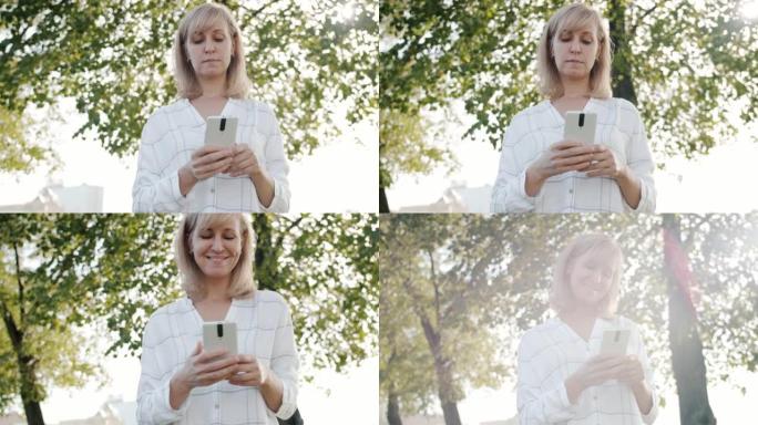 阳光明媚的日子，快乐的成年女性在户外享受智能手机的社交媒体的肖像