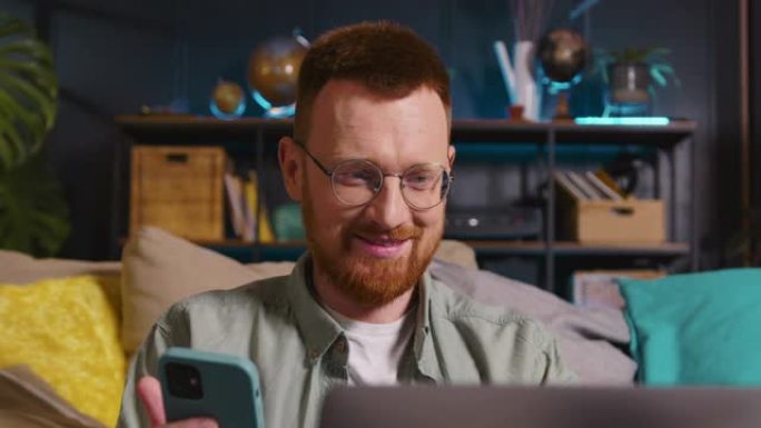 网络安全快乐年轻的白人男性博客作者使用笔记本电脑和智能手机输入密码在家工作。