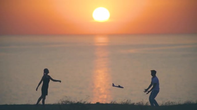 男孩和女孩把玩具飞机扔在日落背景上