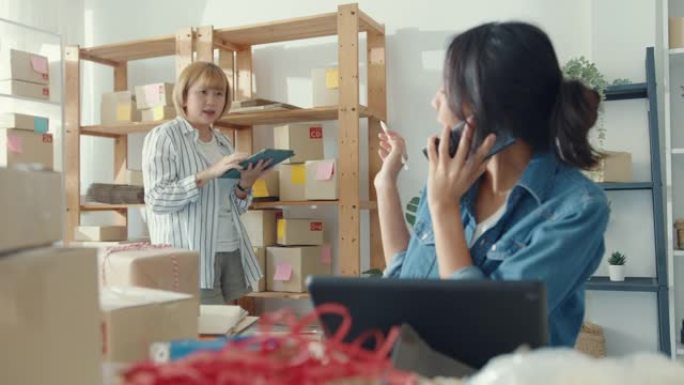 年轻的亚洲女企业家使用手机电话接收采购订单，并在家庭办公室检查库存工作的产品。小企业主，在线市场交付