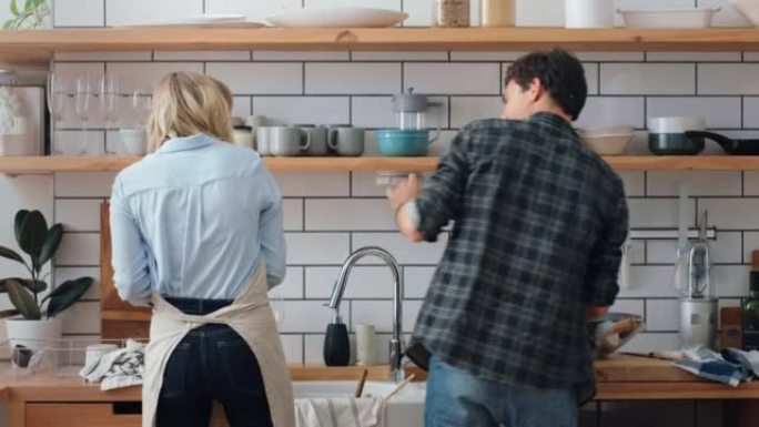 年轻夫妇在厨房里玩肥皂泡，同时在家里的公寓里一起洗碗。快乐，有趣和愚蠢的女人，男人或人们为爱，关怀和