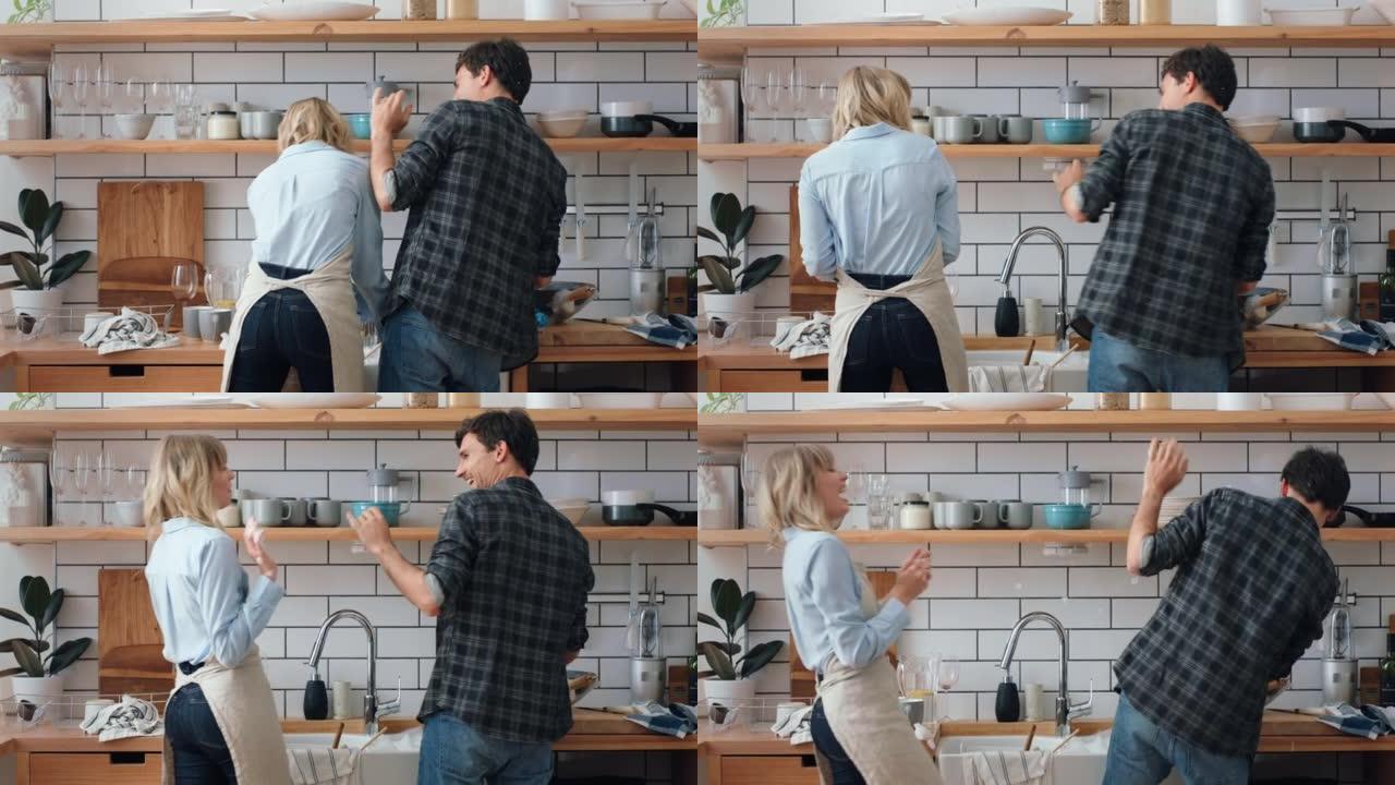 年轻夫妇在厨房里玩肥皂泡，同时在家里的公寓里一起洗碗。快乐，有趣和愚蠢的女人，男人或人们为爱，关怀和