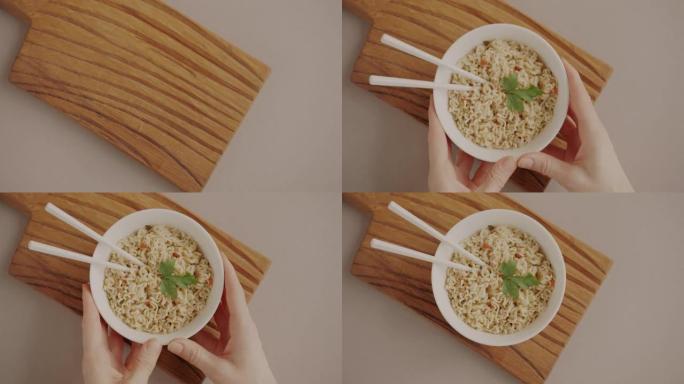 双手在米色背景上放一碗筷子方便面的俯视图