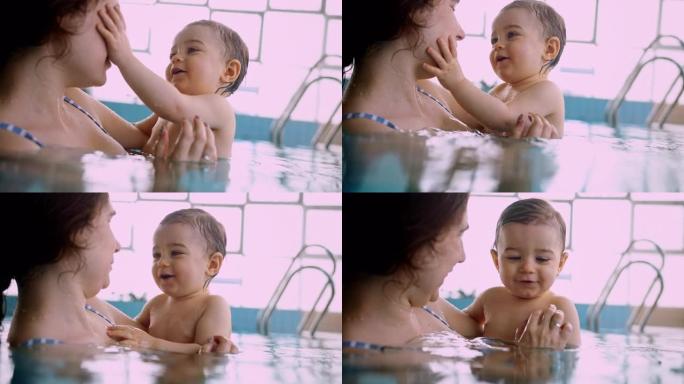 妈妈和快乐的宝宝在室内游泳池里抚摸着微笑的脸