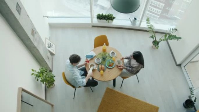 年轻男女吃早餐，坐在厨房的桌子旁聊天的俯视图