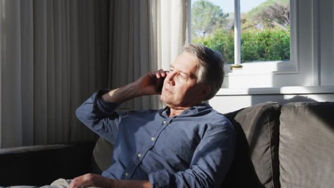 高个子白人坐在阳光明媚的客厅里，用智能手机聊天