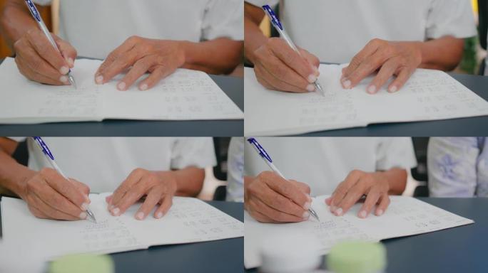 亚洲高级男子在家笔记本上手写血压计和心率的数字