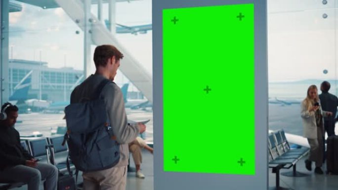 机场航站楼: 年轻人在绿色色度键屏幕上寻找他的飞弹到达出发信息显示。背景: 不同的人在航空枢纽的登机