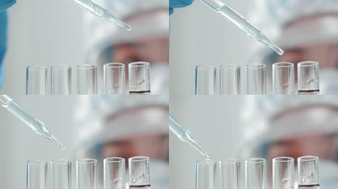 戴着手套和白色实验室外套的女人的手拿着滴管将彩色液体滴入玻璃试管中