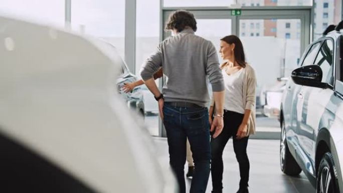 SLO MO汽车推销员在汽车陈列室向一对成熟夫妇展示新车
