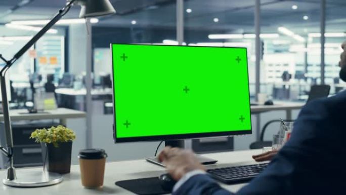 成功的黑人商人坐在办公桌前，在办公室里用绿屏笔记本电脑工作。使用色度键显示的非裔美国商人。肩弧射击