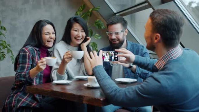 快乐的年轻人在咖啡馆用智能手机拍照时，碰着咖啡杯大笑