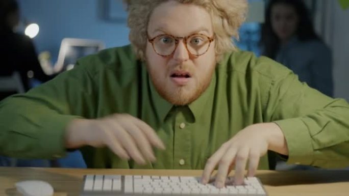 喜剧演员的肖像在匆忙中用电脑打字，用滑稽的脸看着相机