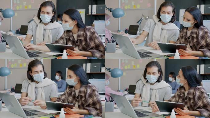 男女同事使用笔记本电脑并在办公室戴着口罩聊天