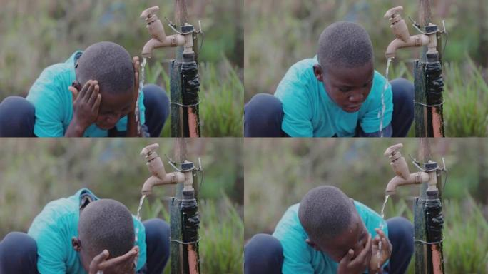 一个非洲黑人小男孩坐在公共水源点上洗脸的特写。水危机。贫困。气候变化。全球变暖。干旱