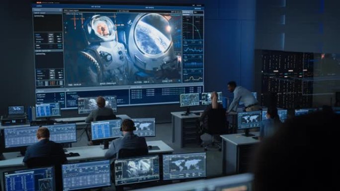 任务控制中心的一群人在大屏幕上与空间站上的宇航员建立了成功的视频连接。飞行控制科学家坐在电脑前。