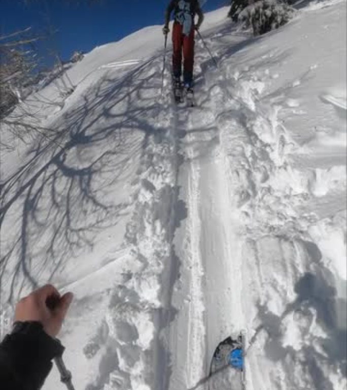 一个朋友在阳光明媚的日子里滑雪上山的垂直视点镜头